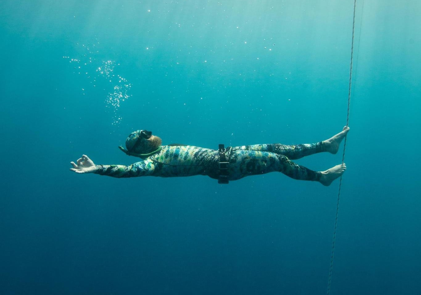 A freediver floating on their back beside the line, arms out, at ease