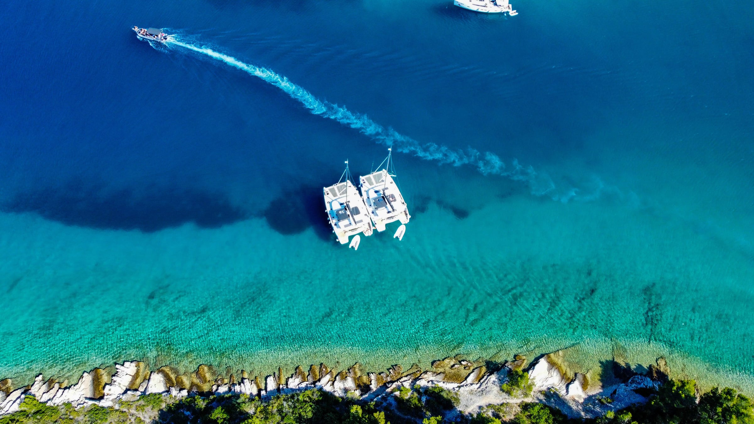 Two catamarans moored in clear water off a rocky coast