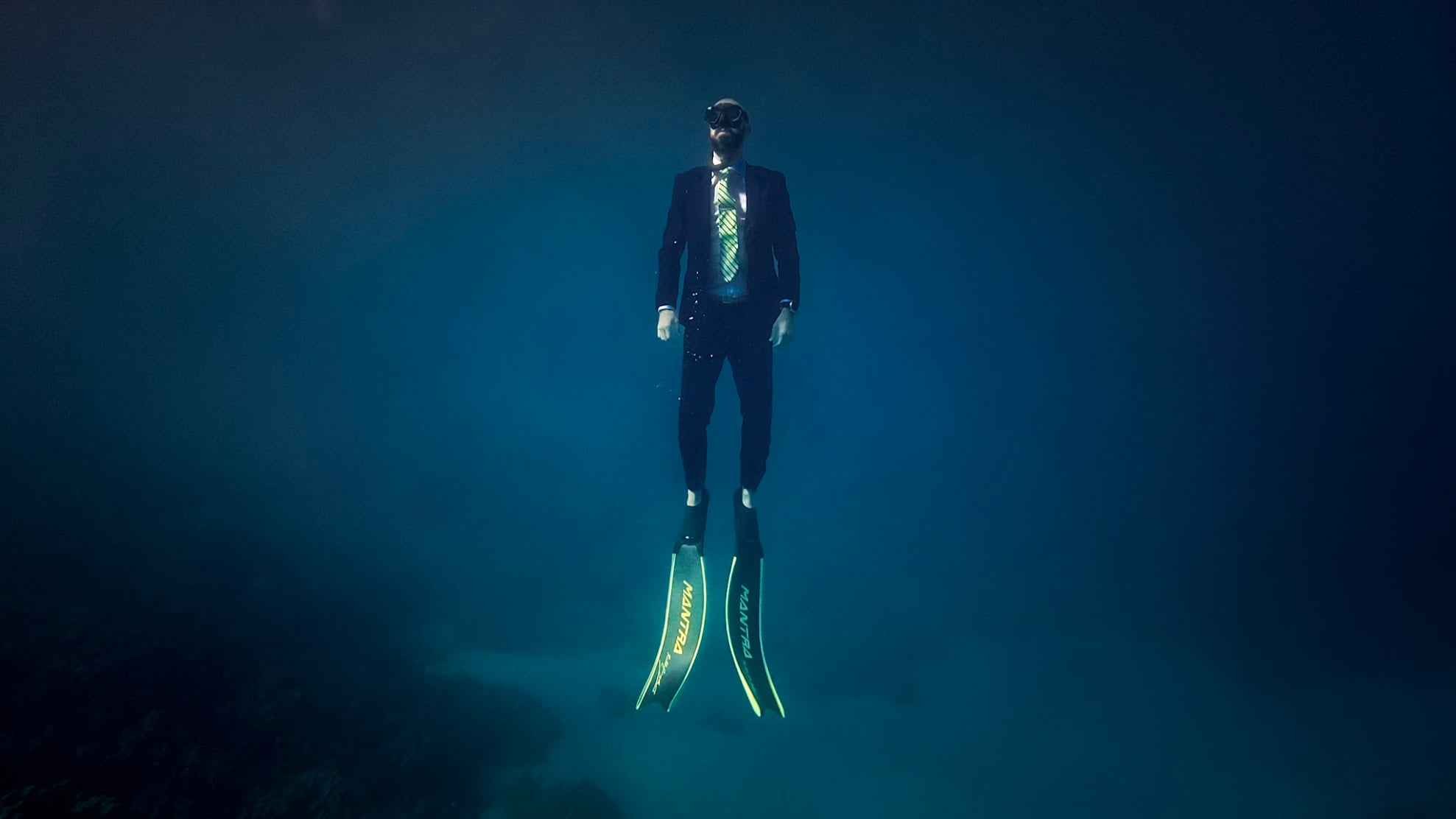 Costa rising through deep blue water in a business suit and long fins, on one breath