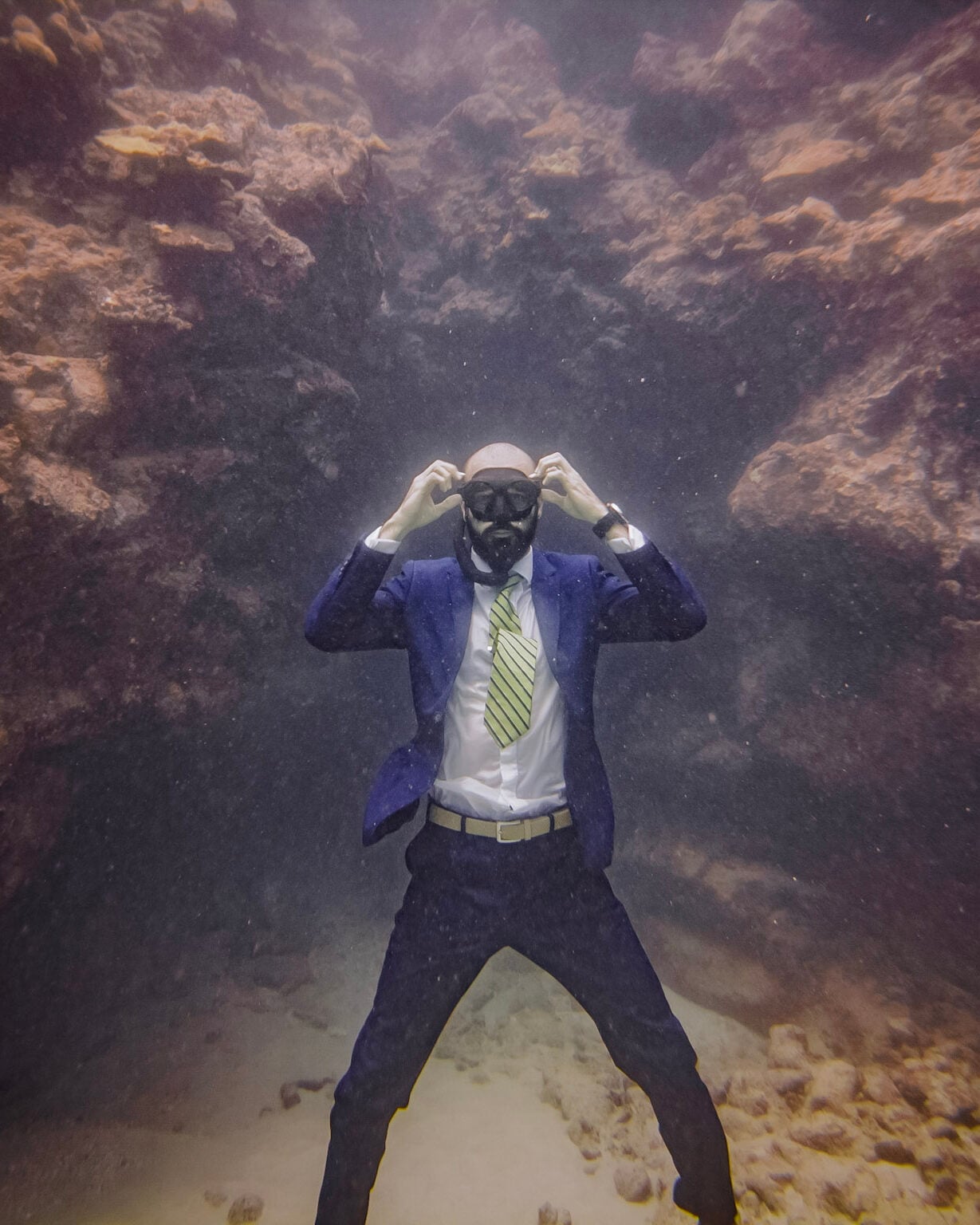 Costa standing on the sea floor in a business suit, hands on his mask