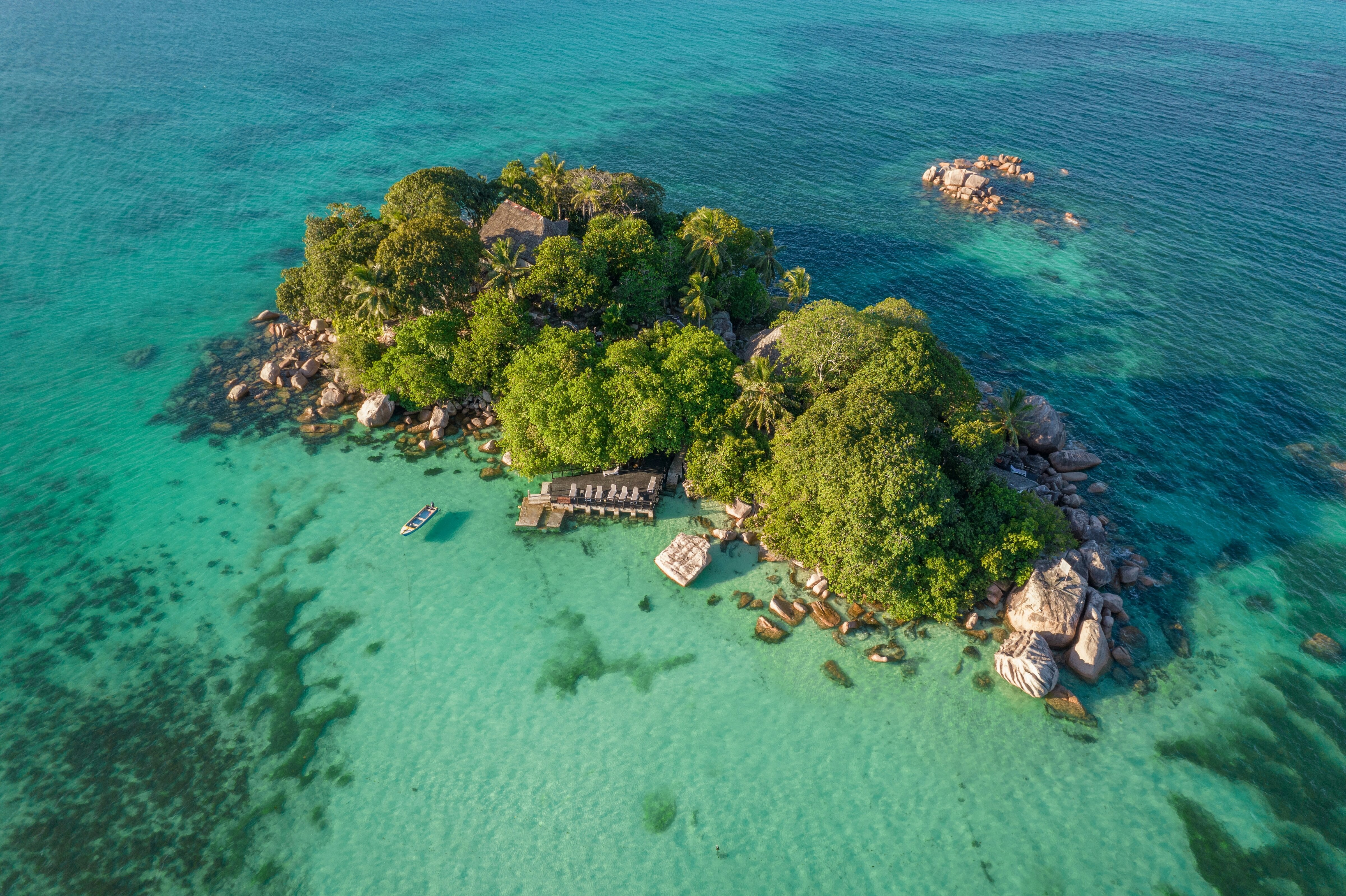 A small granite island in the Seychelles from above, palms and a wooden jetty on a turquoise lagoon