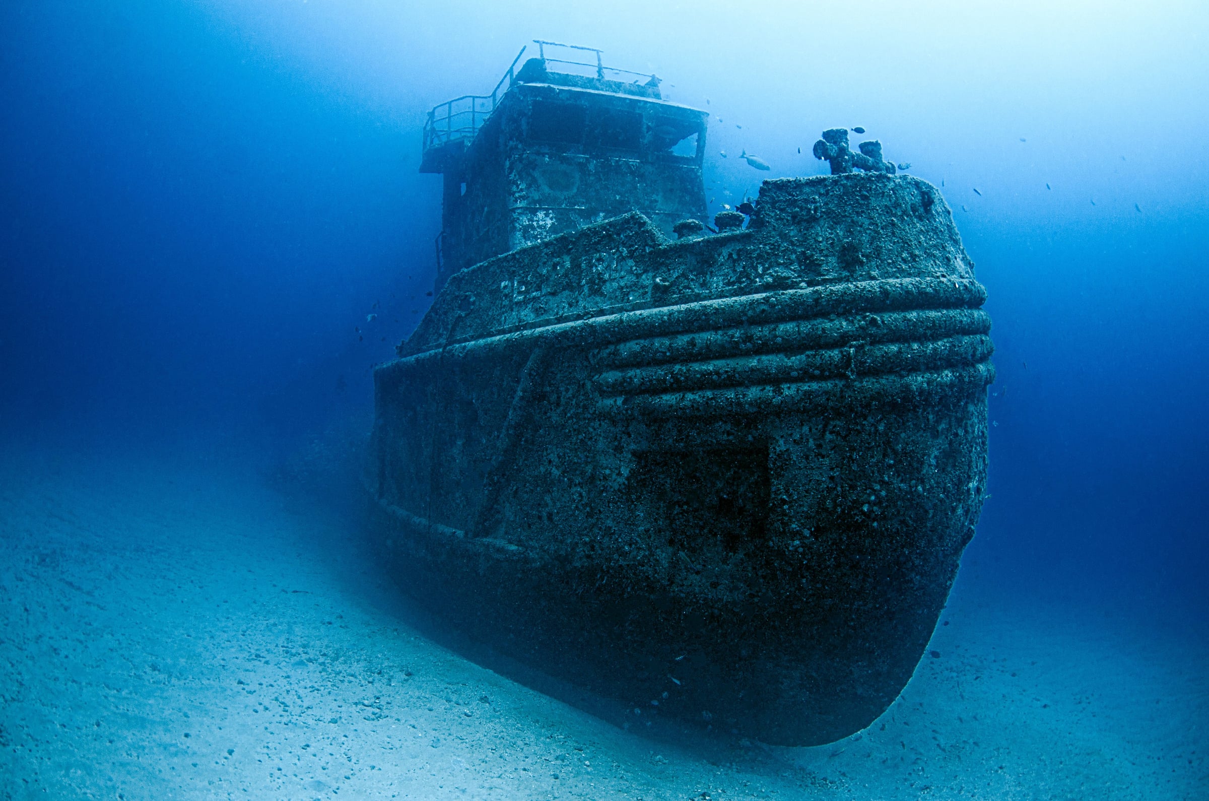 A sunken ship standing upright on the sand in deep blue water, its wheelhouse rising toward the light
