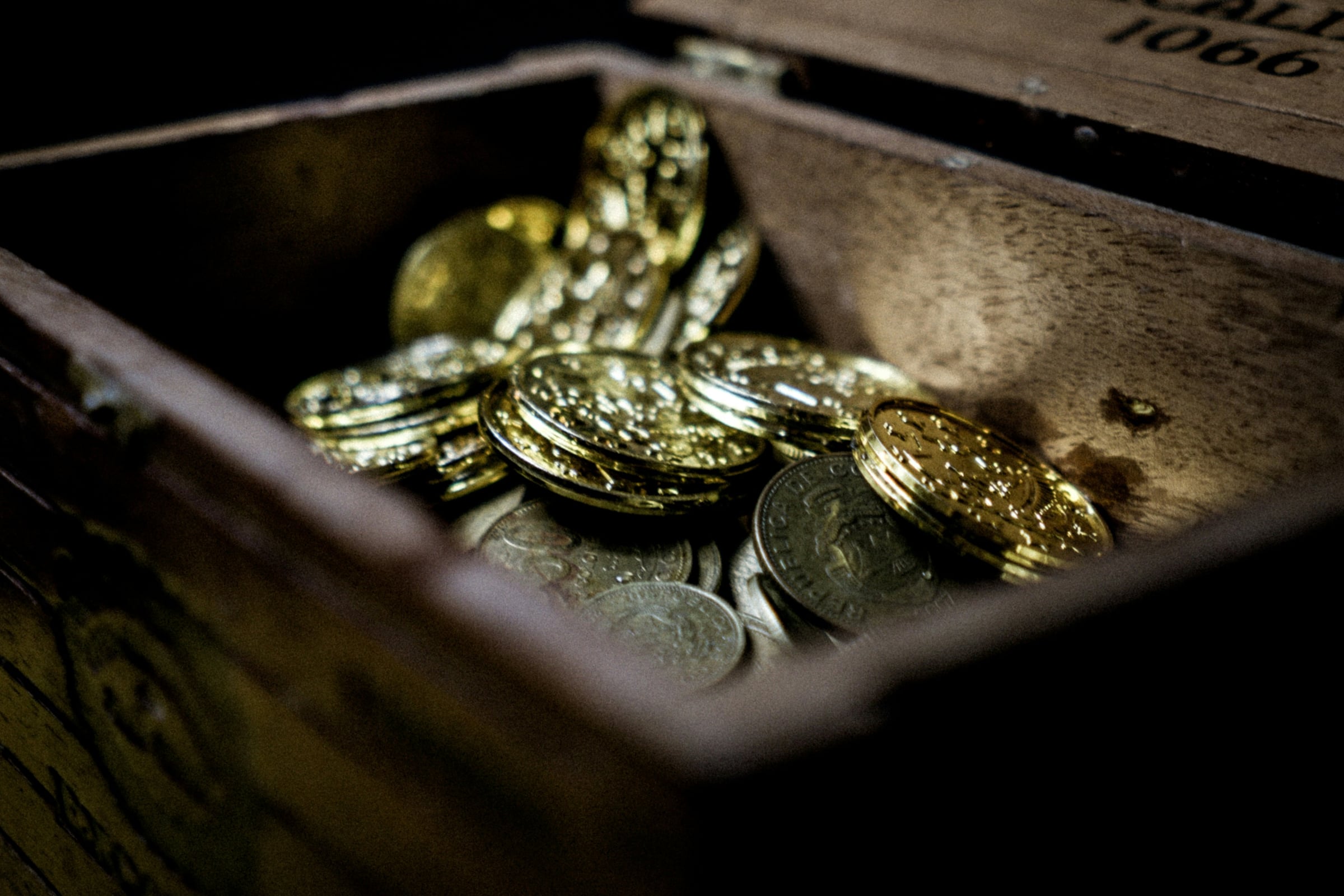 An open wooden chest of gold coins in lamplight